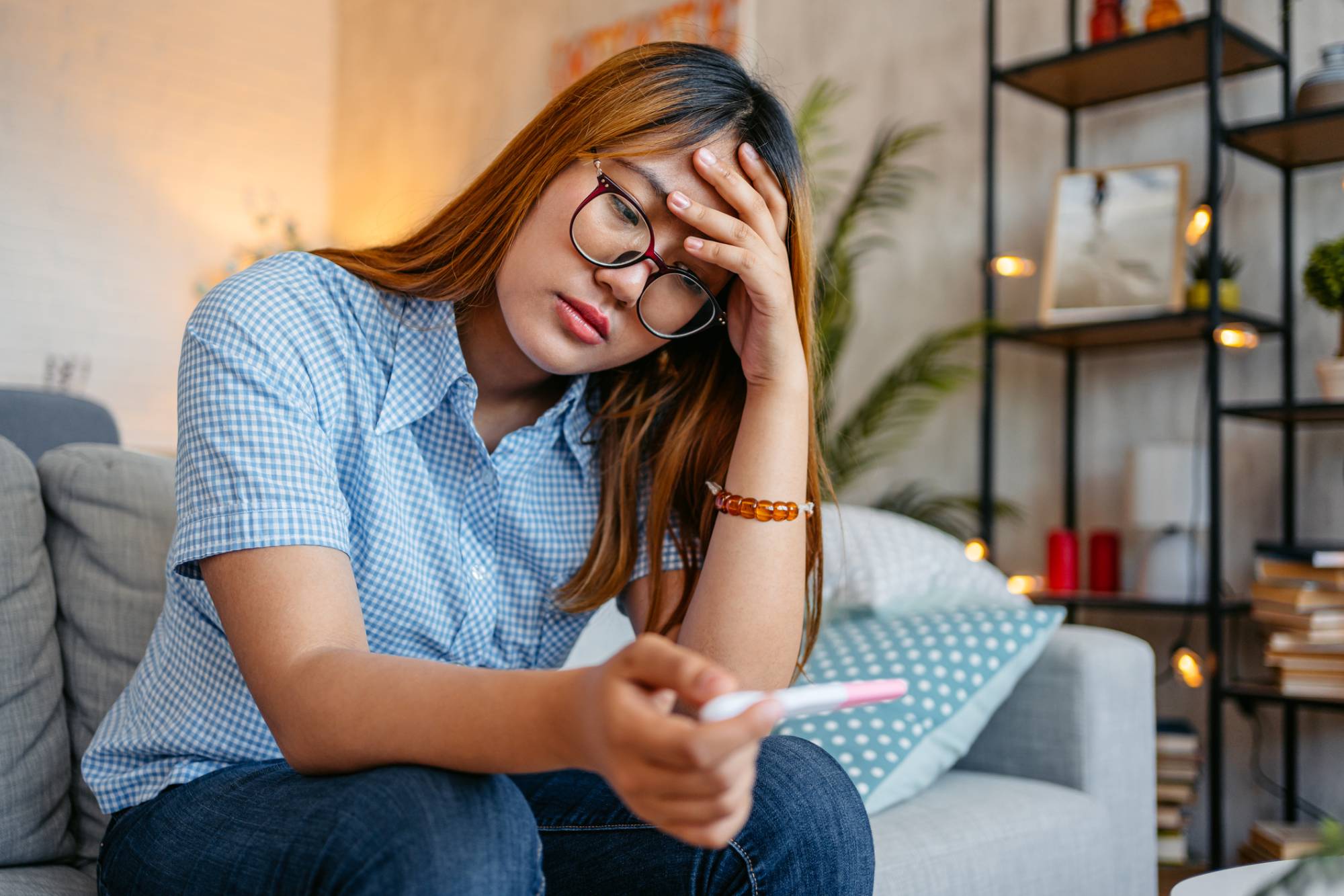 woman sitting down holding pregnancy test looking distraught and sad