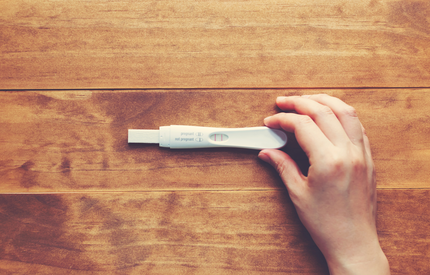 Woman,Holding,A,Positive,Pregnancy,Test,On,A,Wooden,Desk