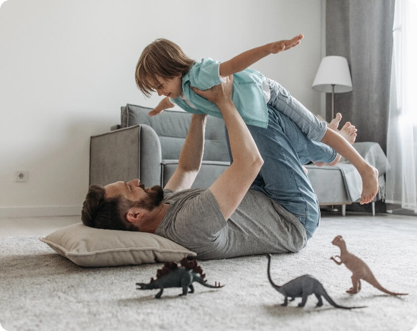 Father and son playing with dinosaurs in the living room.