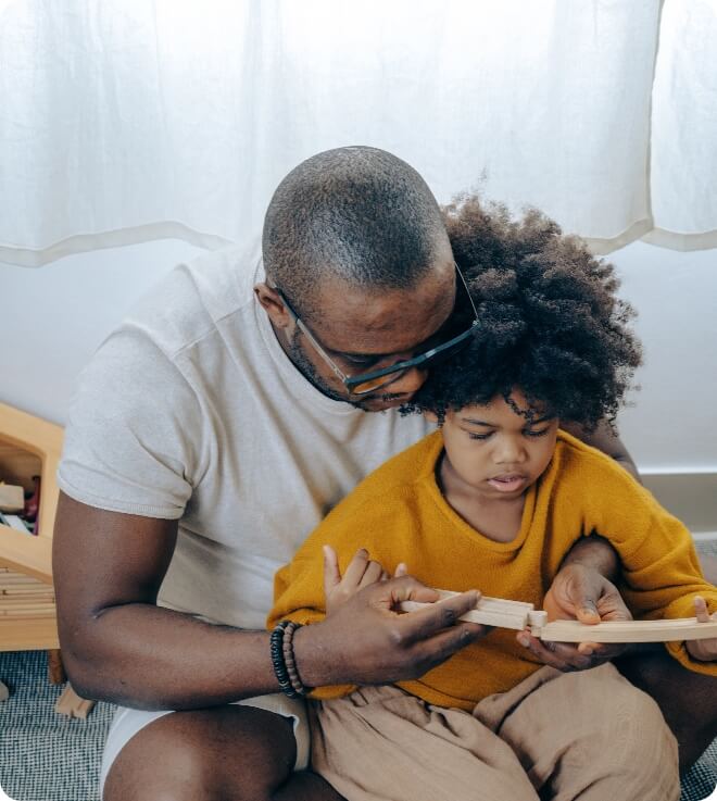 An african-american man reading a book to his child.