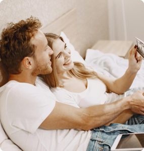 A man and woman laying on a bed with a tablet in their hands.